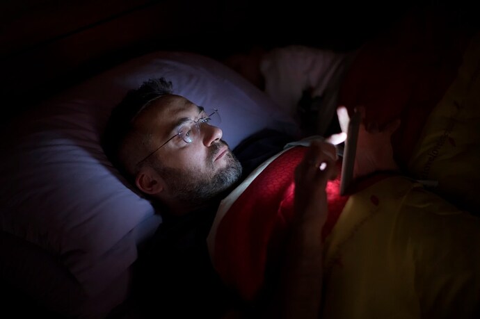 Image 4: A man in glasses lies in bed, illuminated by the soft glow of his smartphone screen.